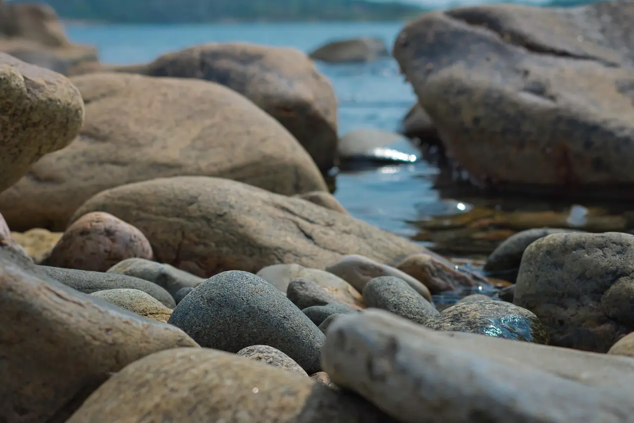 Runda stenar vid strandkant med lugnt vatten i bakgrunden